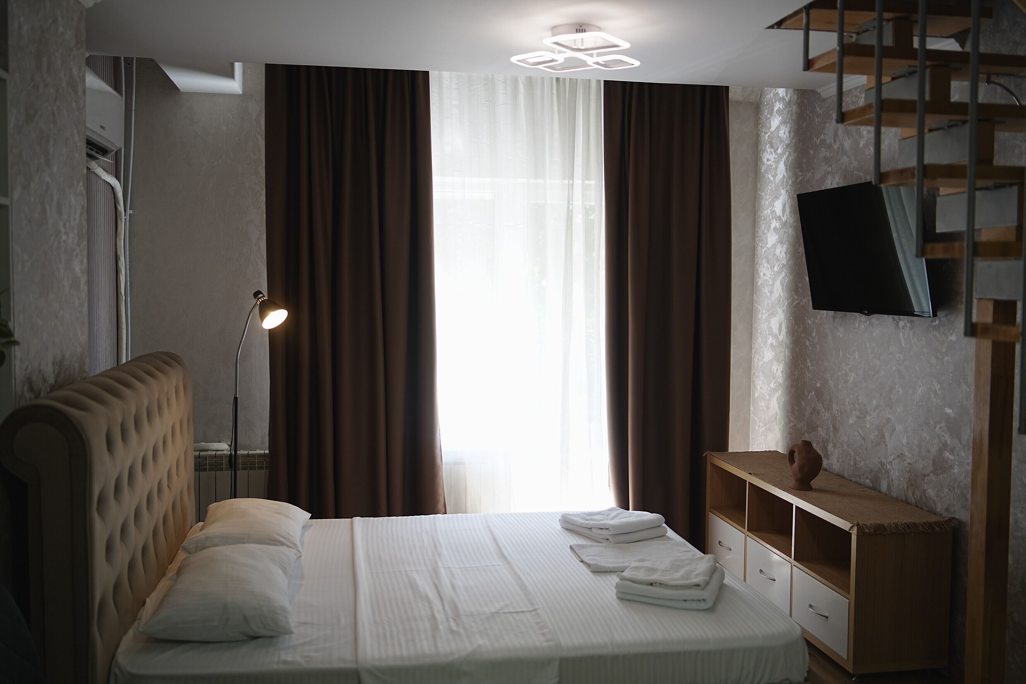 A hotel room with a bed, a desk, a flat-screen TV, and a window with curtains.