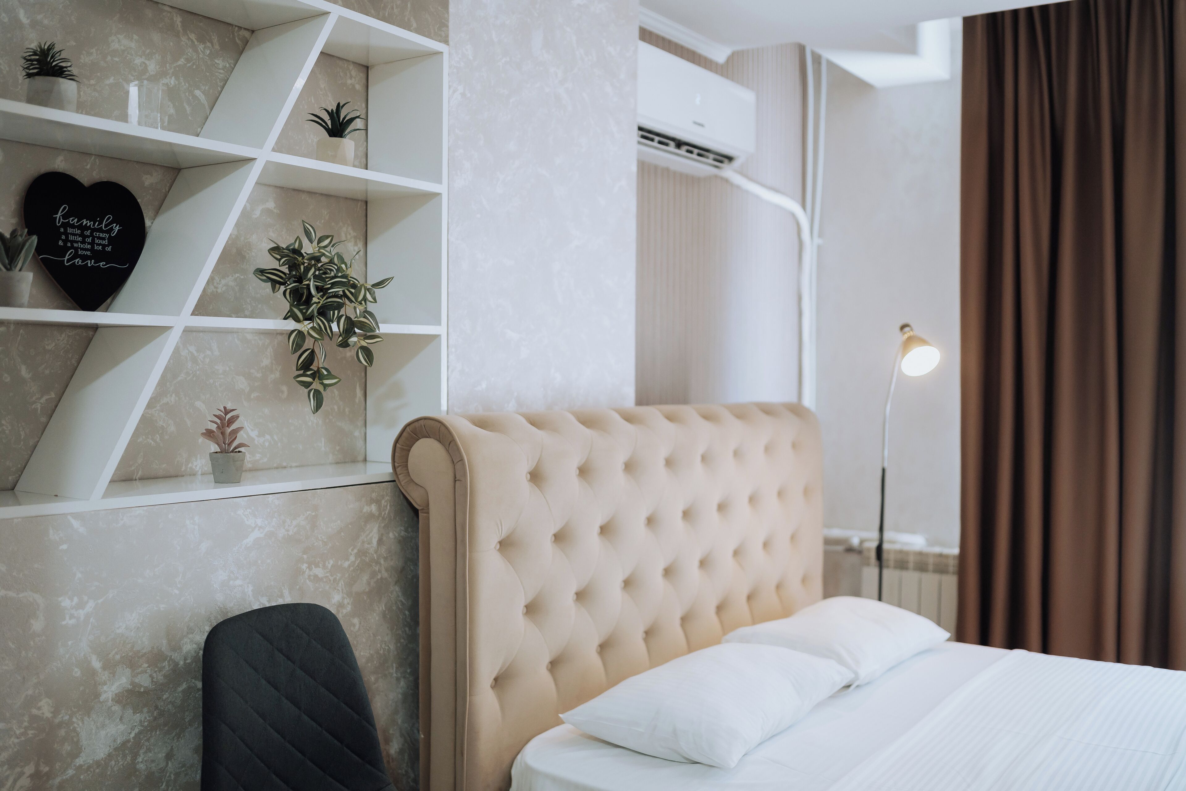 A modern bedroom with a tufted headboard, a bedside lamp, and a shelf with decorative items.