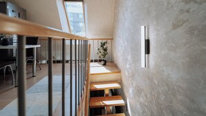 A modern interior with a wooden staircase, a potted plant, and a view of the outside through a skylight.