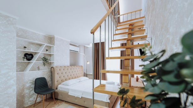 A bedroom with a bed, a chair, a wooden desk, shelves with plants, and a staircase.