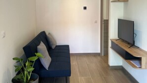Een moderne woonkamer met een donkerblauwe bank, een potplant en een televisie op een houten plank.