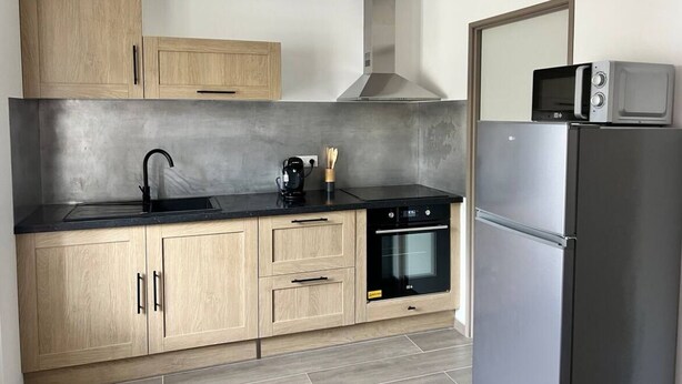 Een moderne keuken met lichte houten kastjes, een zwart aanrecht, een roestvrijstalen koelkast en een inbouwoven.