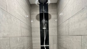 Een moderne badkamer met een douchecabine van glas, betegelde wanden en een zichtbare afvoer.