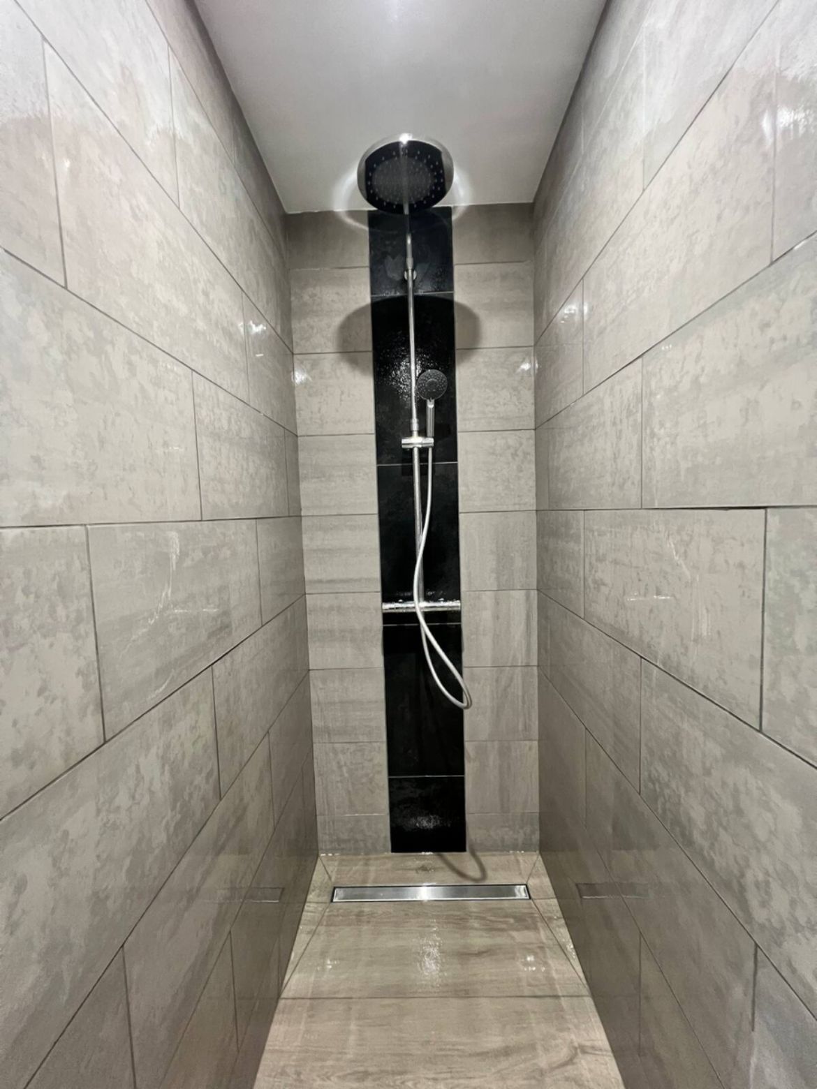 Un baño moderno con ducha acristalada, paredes alicatadas y desagüe visible.