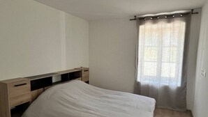 Een slaapkamer met een bed, een houten hoofdbord, ingebouwde lades en een raam met gordijnen.
