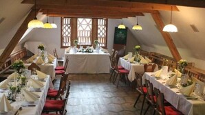 Un comedor con varias mesas dispuestas para una comida, vigas de madera en el techo y un ventanal con diseño de celosía.