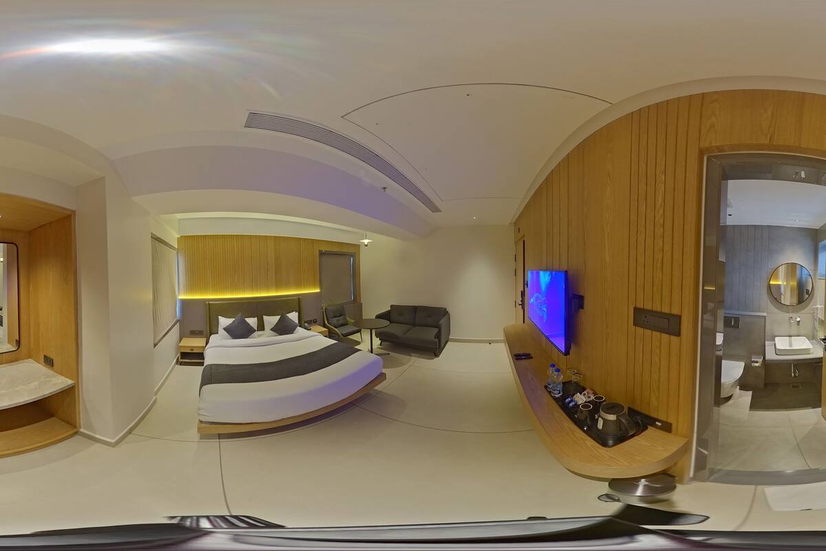 A modern hotel room with a curved bed, a TV, a bathroom, and a wooden accent wall.