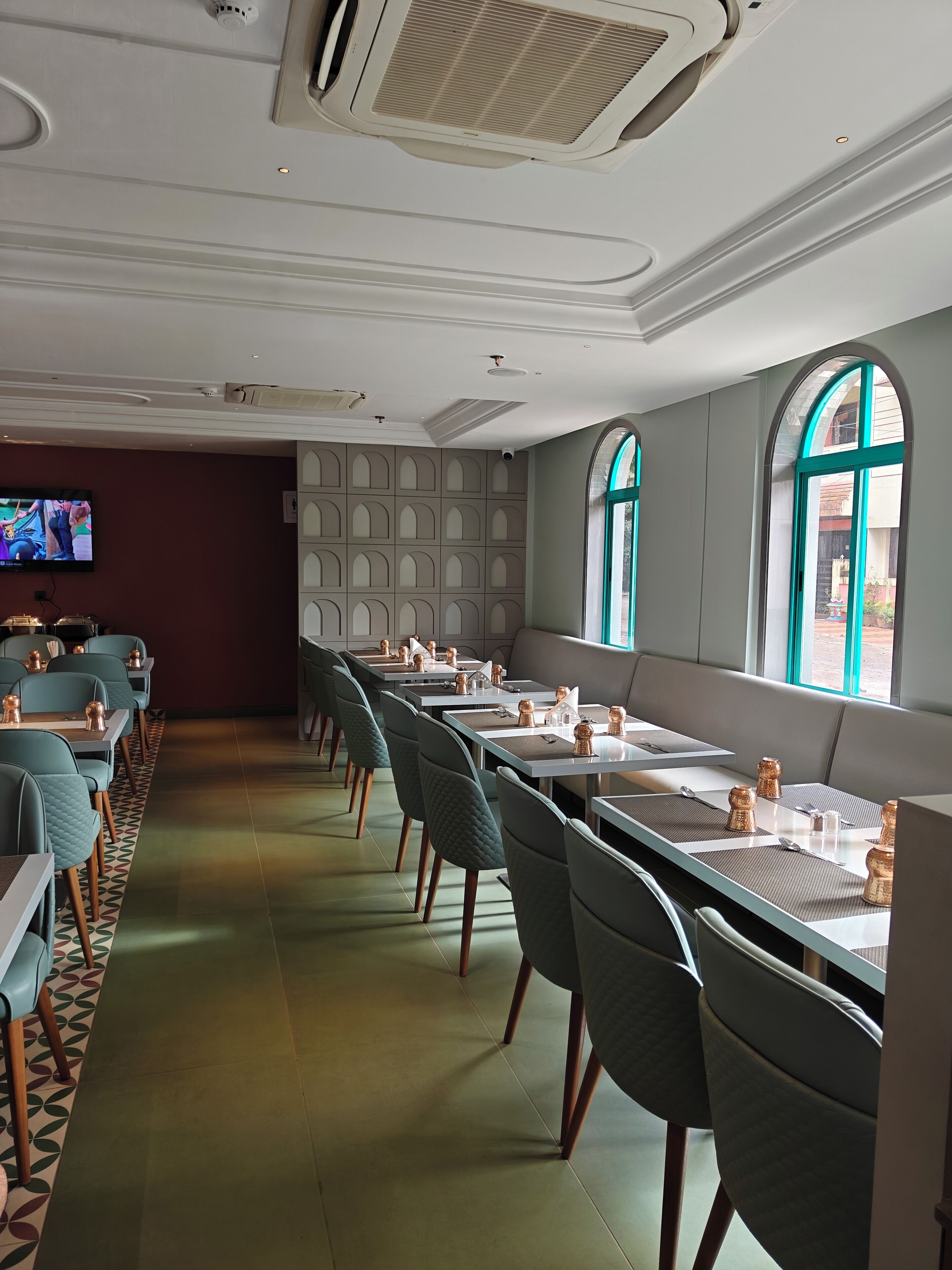 A restaurant with long tables, teal chairs, and a TV on the wall.