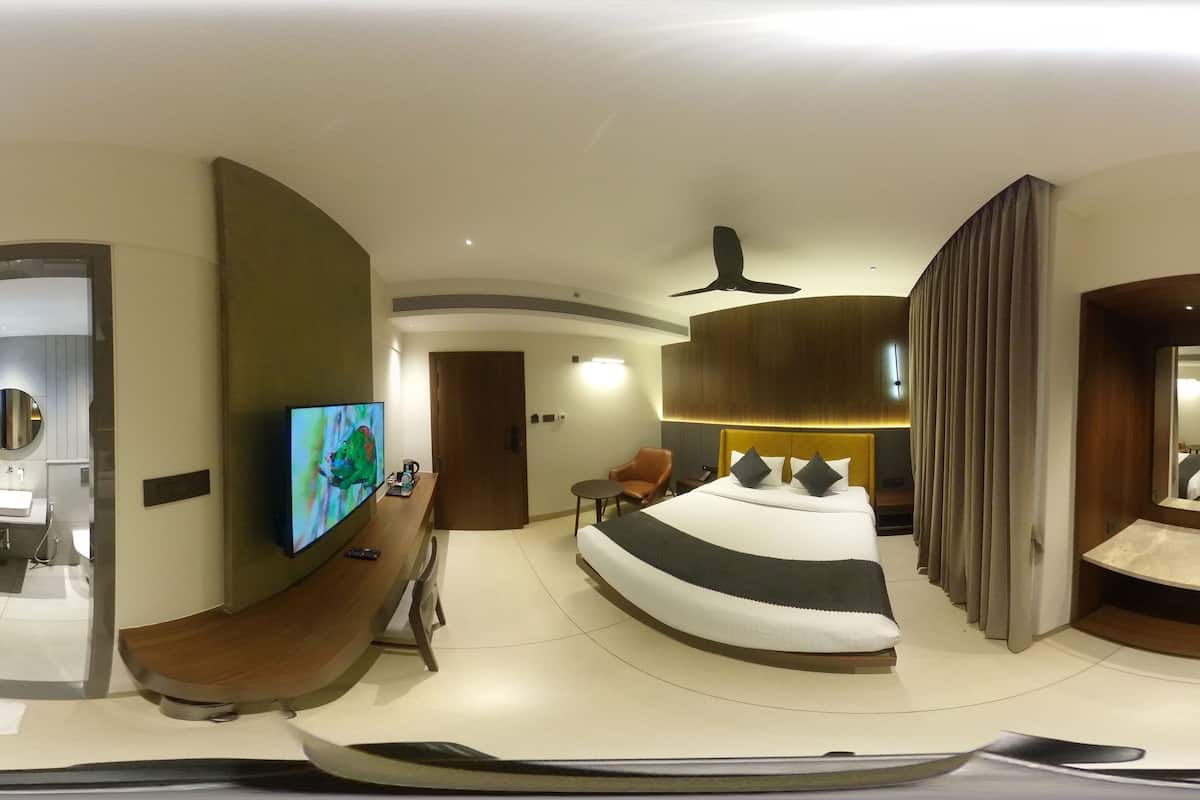 A modern hotel room with a curved bed, a television, a bathroom, and a mirror.
