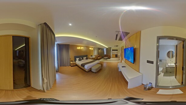Ein modernes Hotelzimmer mit einem großen Bett, einem Fernseher, einem Schreibtisch und einem durch eine Glastür einsehbaren Badezimmer.