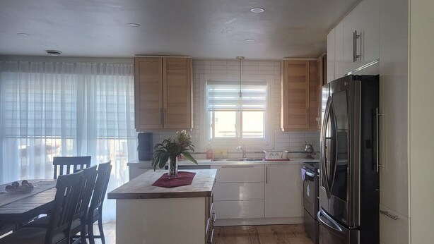 A compact kitchen with wooden cabinets, a stainless steel refrigerator, and a dining area with a table and chairs.