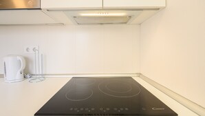 A modern kitchen with a black induction cooktop, a white kettle, and a stainless steel range hood.