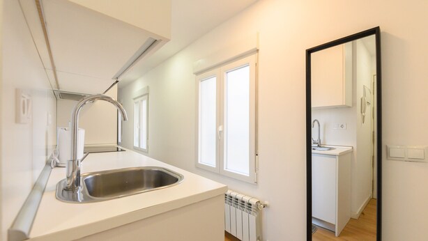A modern kitchen with a stainless steel sink, white cabinetry, and a large mirror reflecting the room.