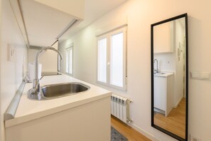 Una cocina moderna con un lavamanos de acero inoxidable, armarios blancos y un espejo grande que refleja el ambiente.