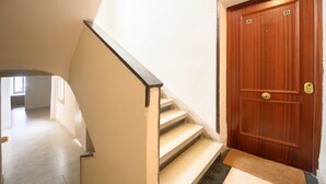 A wooden door with a brass handle, a carpeted entrance, and a staircase with beige steps leading to an upper floor.