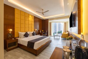 A modern hotel room with a large bed, a desk with a coffee maker, a TV, and a view of high-rise buildings. - Saltstayz Premier - Manesar & Sector 86 (Gurugram)