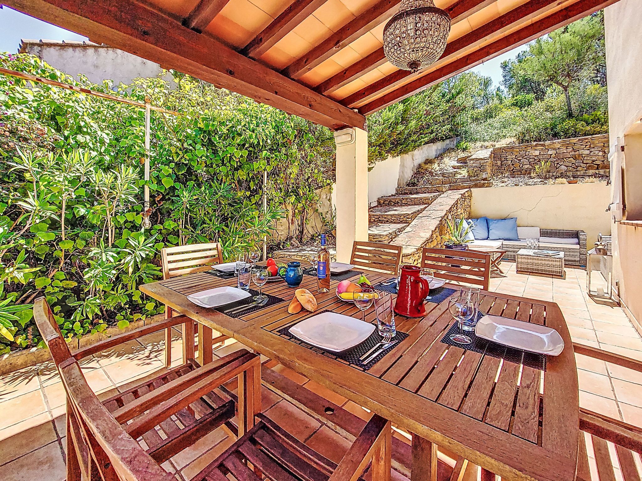 An outdoor dining area with wooden tables and chairs, surrounded by lush greenery and a stone staircase.