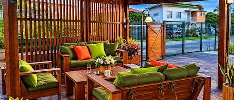 Un área de estar al aire libre con mobiliario de madera y una pérgola de madera.