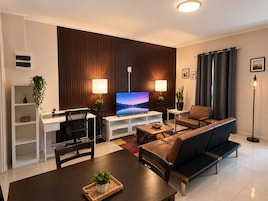 Uma sala de estar moderna com televisão de tela plana, sofá, mesa de jantar e um espaço de trabalho com escrivaninha e cadeira.