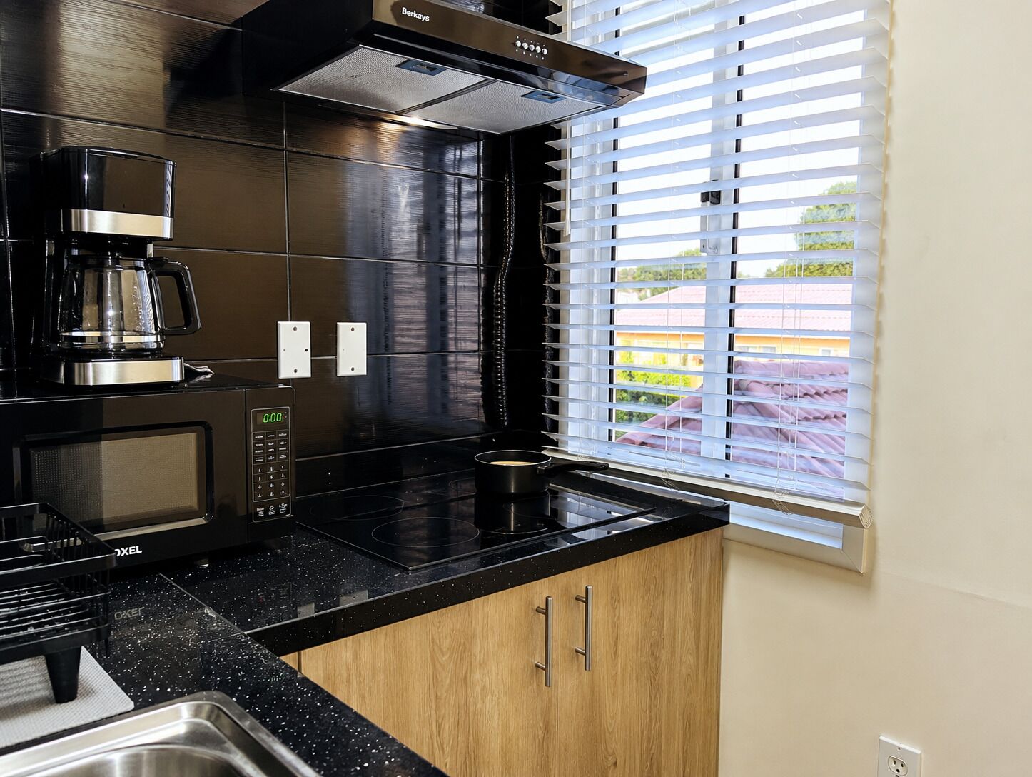 A modern kitchen with a black countertop, stainless steel appliances, and a window with blinds.