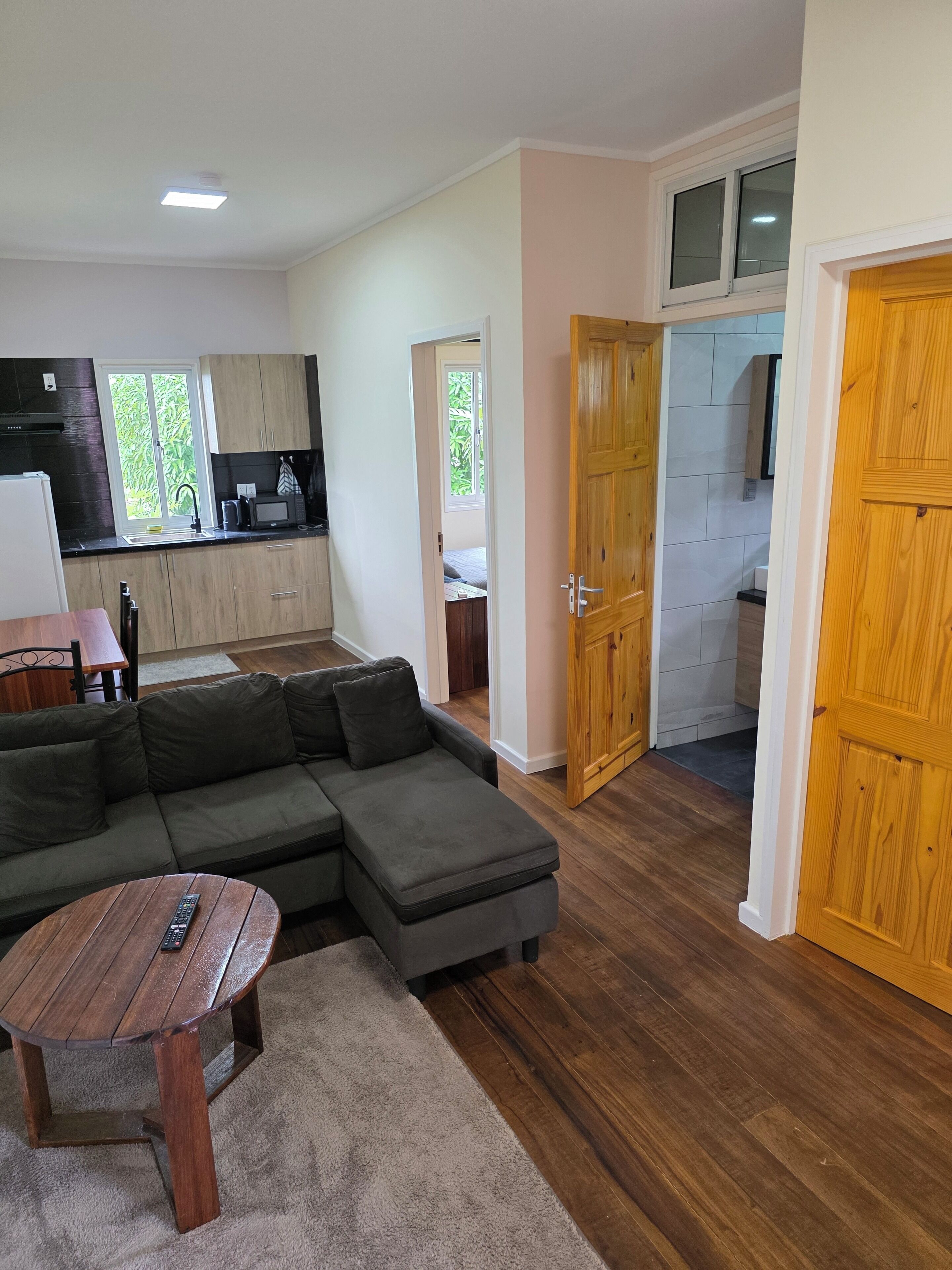 Una sala de estar moderna con un sofá modular, una mesa de centro de madera y una cocina con armarios de madera y una ventana.