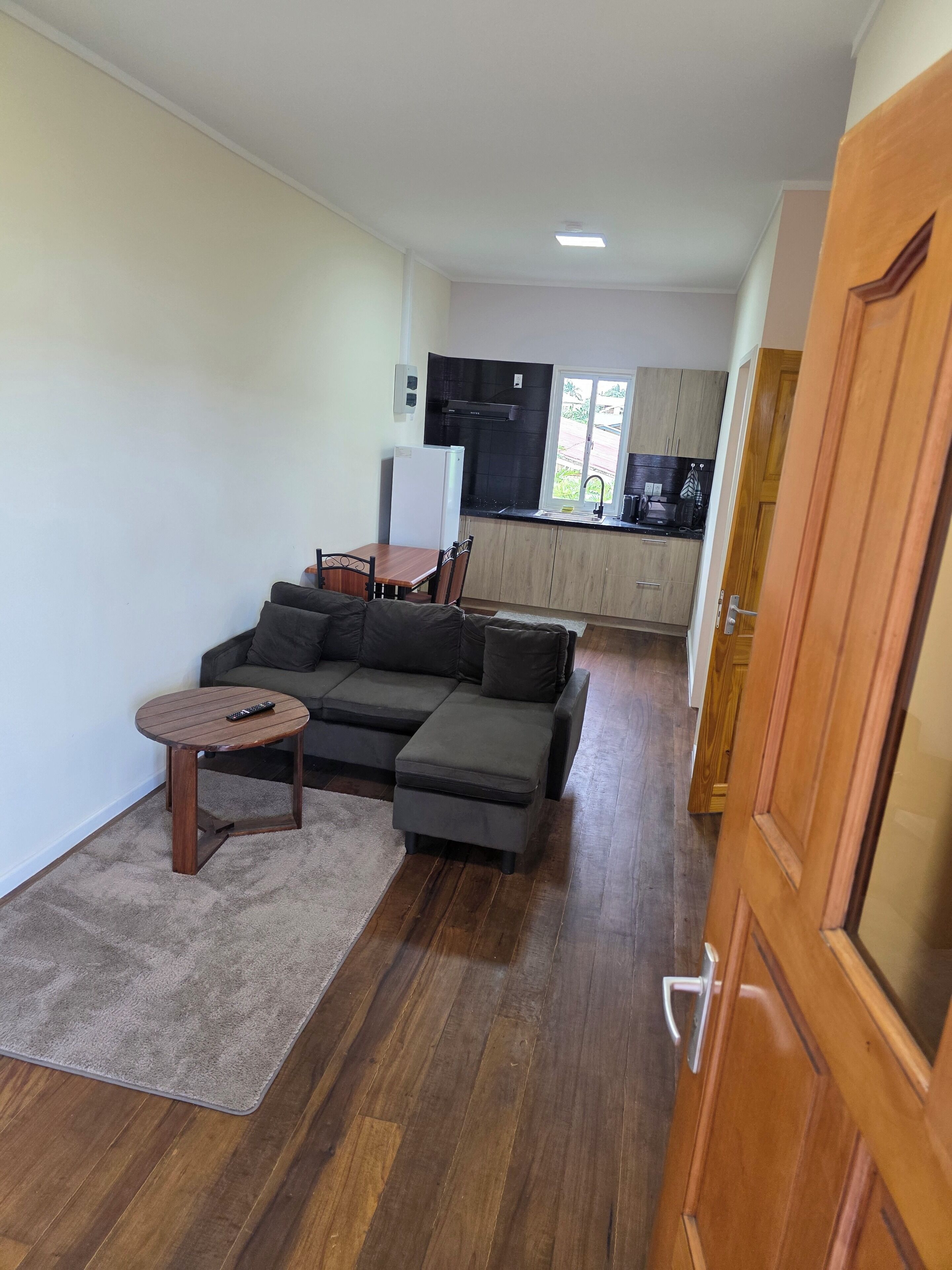 A living room with a sectional sofa, a small round table, and a kitchen in the background.
