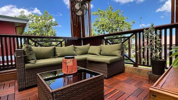An outdoor deck with a wicker sofa, a glass-top coffee table, and a potted plant.