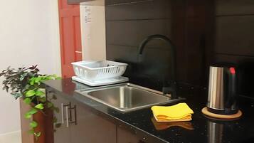 Una cocina moderna con armarios oscuros, un lavamanos de acero inoxidable, una tetera y una planta.