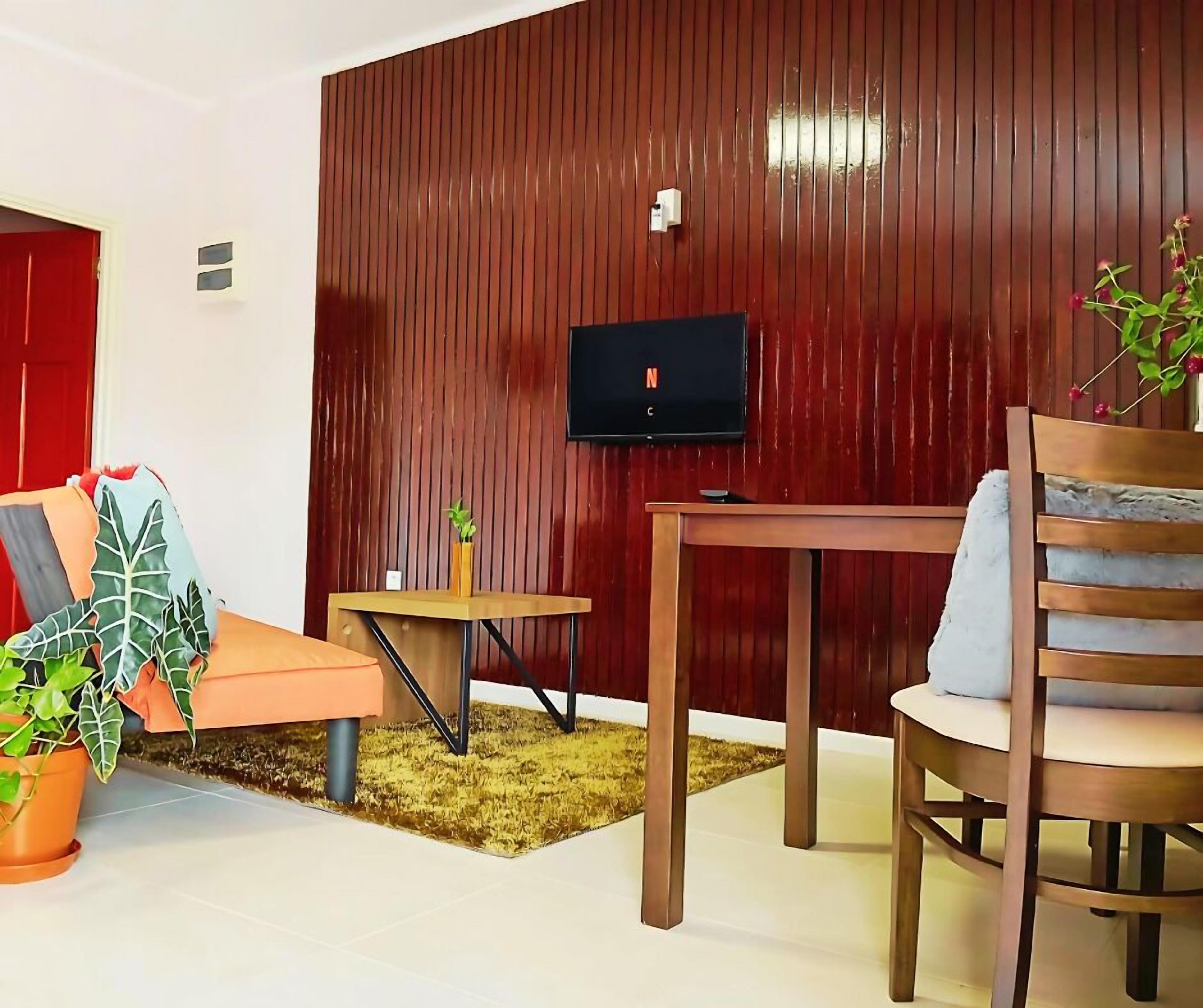 A cozy living room with a red wall, a television, a wooden table, a sofa, and a chair.