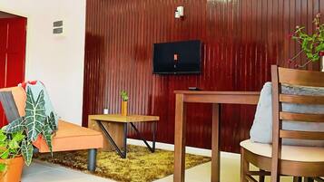 A cozy living room with a red wall, a television, a wooden table, a sofa, and a chair.
