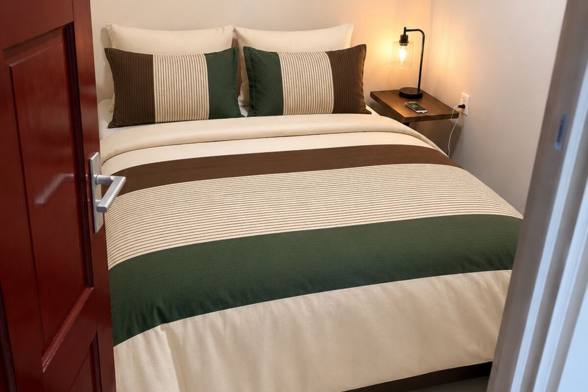 Une chambre à coucher avec un lit, des oreillers, une table de chevet avec une lampe et une porte.