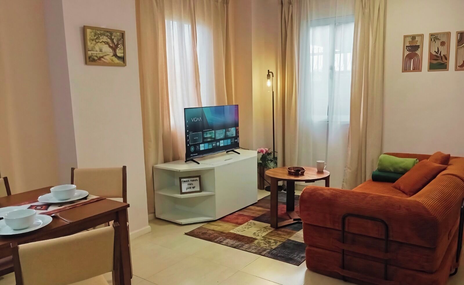 A living room with a TV, a dining table with chairs, a sofa, and a small table with a cup.