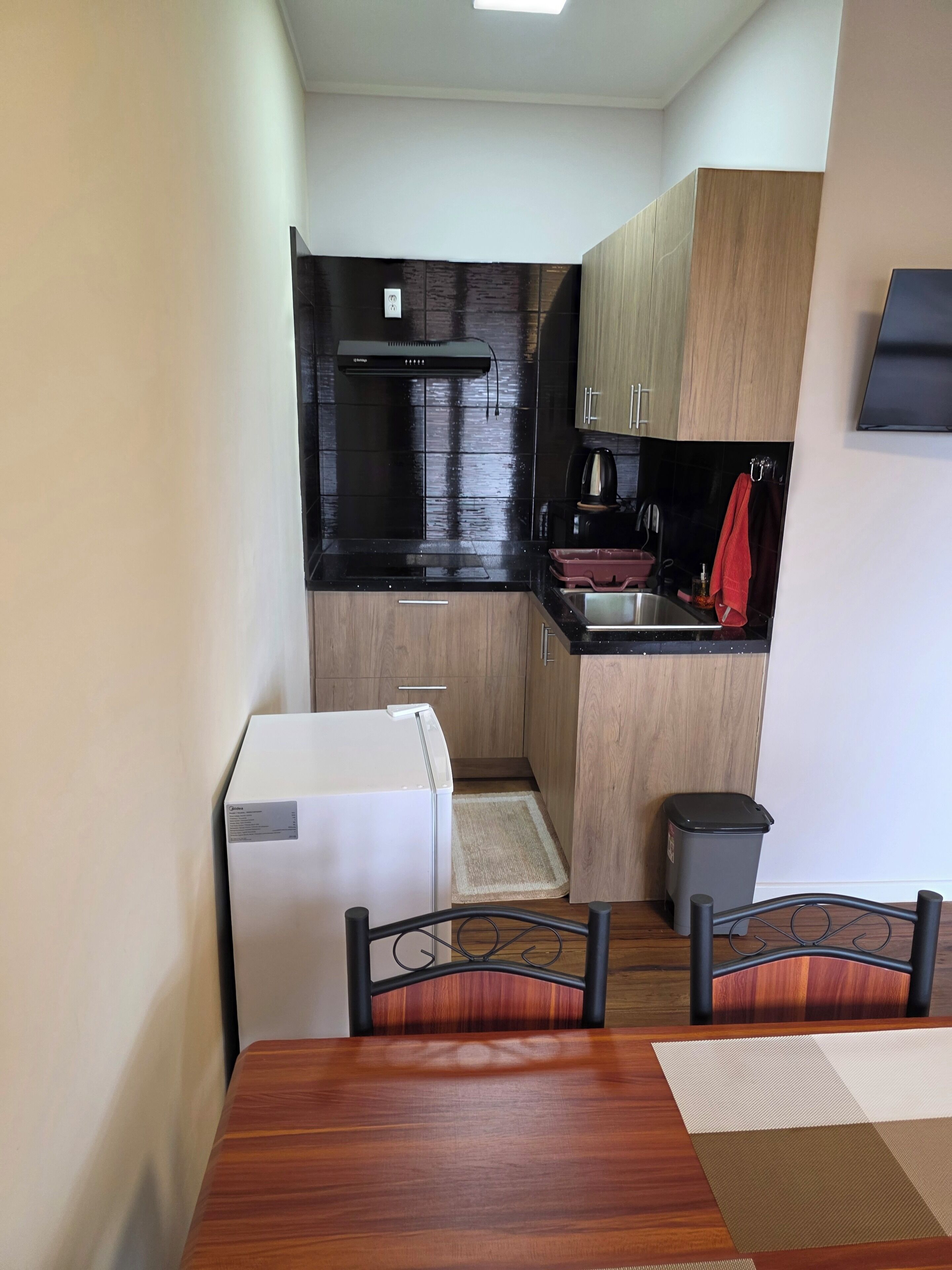 A compact kitchen with a refrigerator, stove, and sink. There is a dining table with chairs and a small trash bin.