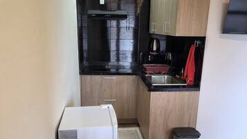 A compact kitchen with a refrigerator, stove, and sink. There is a dining table with chairs and a small trash bin.