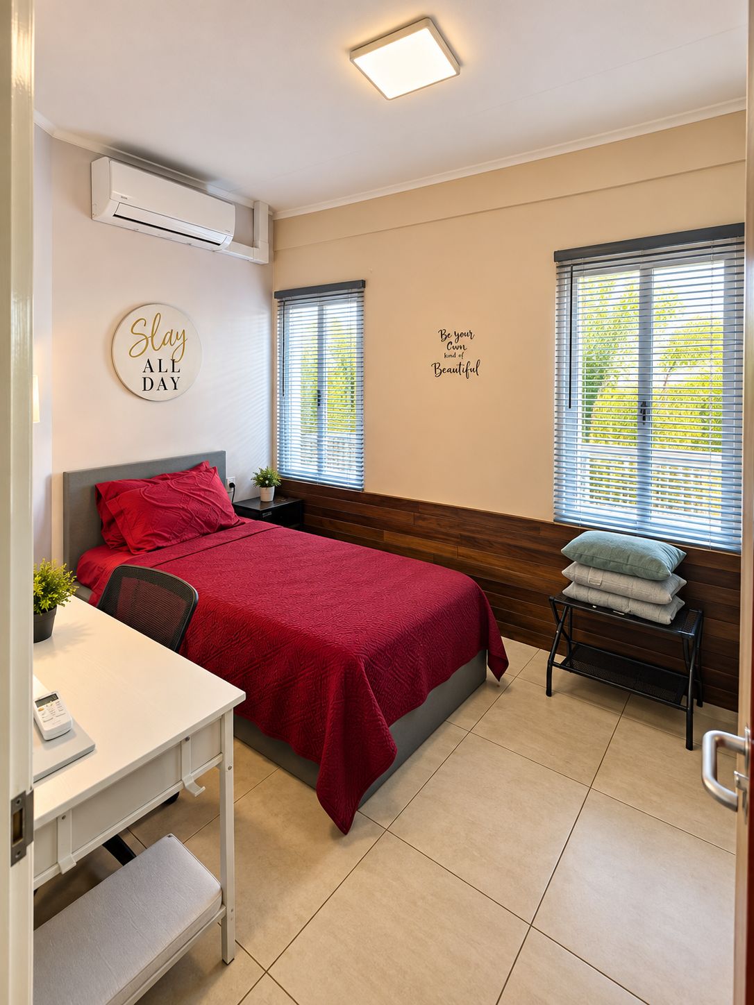 A hotel room with a bed, a desk, a chair, an air conditioning unit, and two windows with blinds.