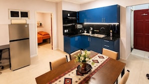 A compact kitchen with blue cabinets, a stainless steel refrigerator, and a dining area with a table and chairs. - Dolfijn Studios (Paramaribo)