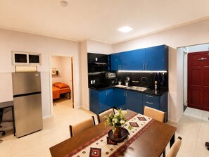 Une cuisine compacte avec des meubles bleus, un réfrigérateur en acier inoxydable et un coin repas comprenant une table et des chaises.
