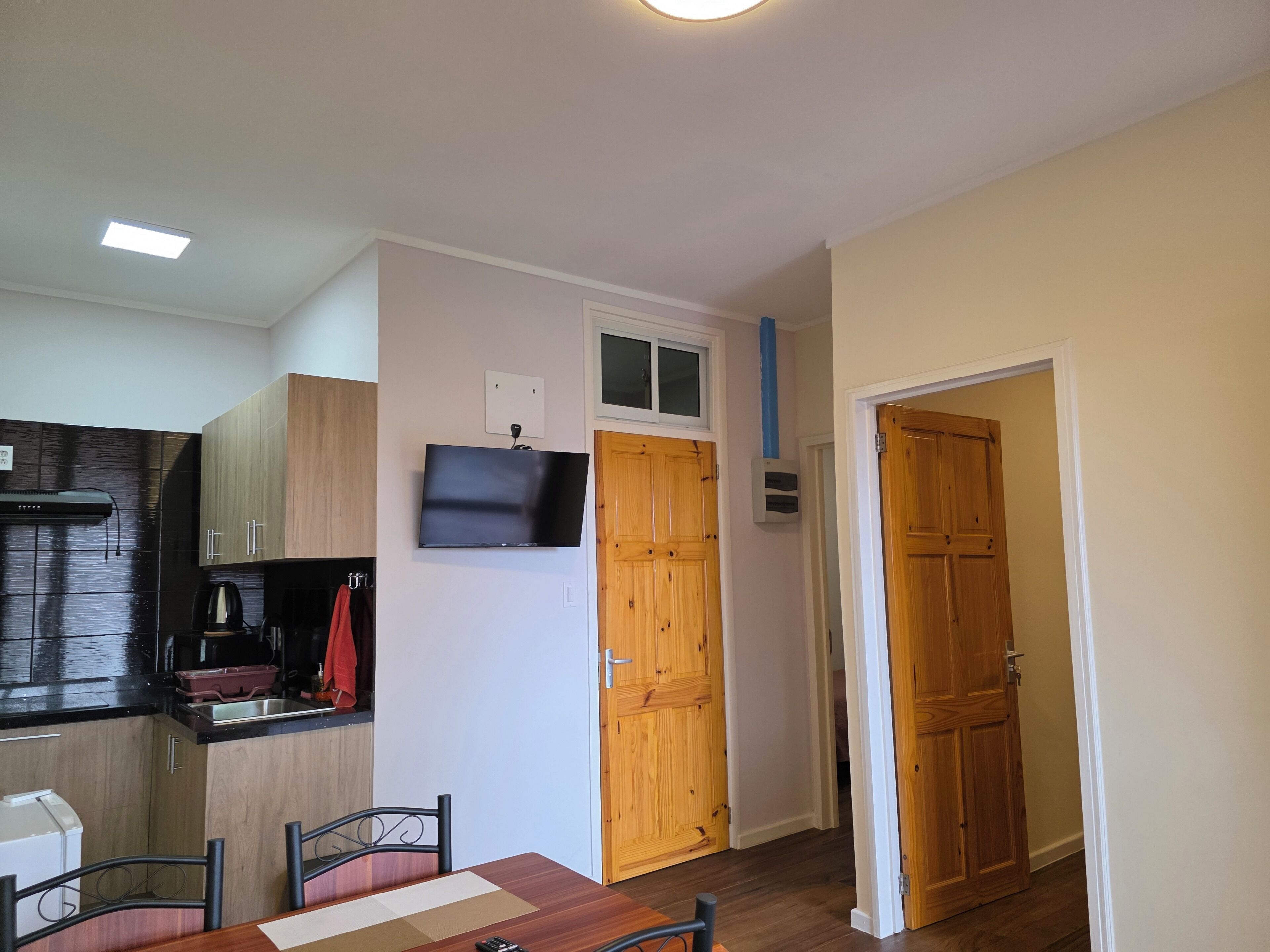 A modern kitchen with a flat-screen TV, wooden cabinets, and a dining area with a table and chairs.
