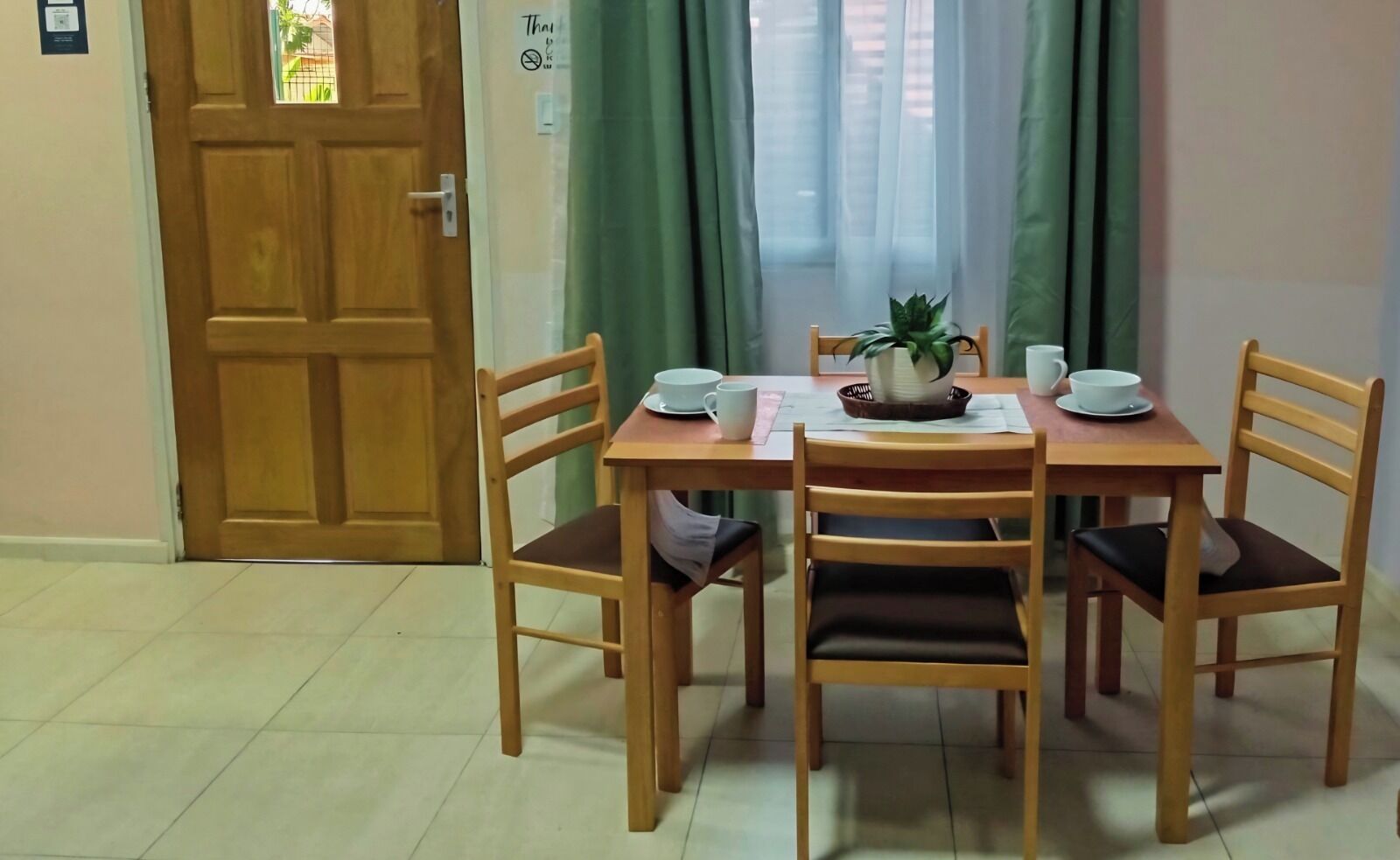 A dining area with a wooden table and chairs, a potted plant, and a door with a sign.