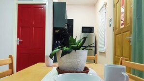 A dining area with a red door, a microwave, a potted plant, and a table with chairs and bowls. - Dolfijn Studios (Paramaribo)