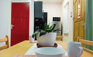 Uma sala de jantar com uma porta vermelha, micro-ondas, planta em vaso e uma mesa com cadeiras e tigelas.