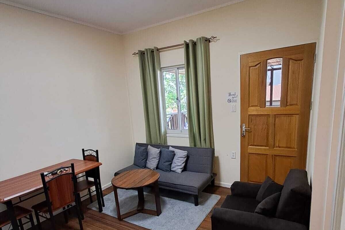 Un espace de vie compact comprenant une table à manger, des chaises, un canapé, une petite table ronde et un divan noir.