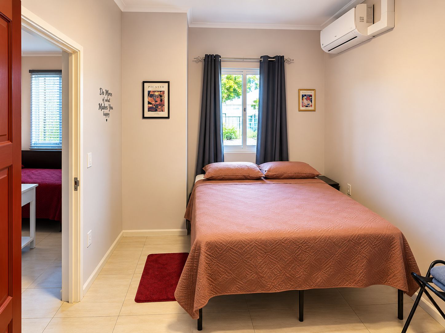 A bedroom with a bed, a red rug, a window with curtains, and wall art.