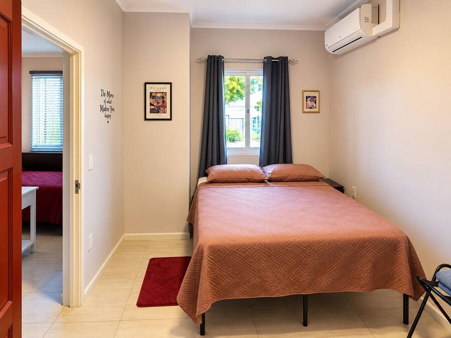 A bedroom with a bed, a red rug, a window with curtains, and wall art.