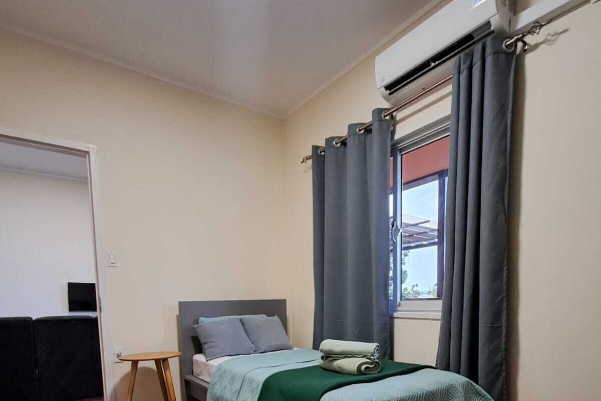 Une chambre à coucher avec un lit, une petite table, une fenêtre avec des rideaux et une porte.