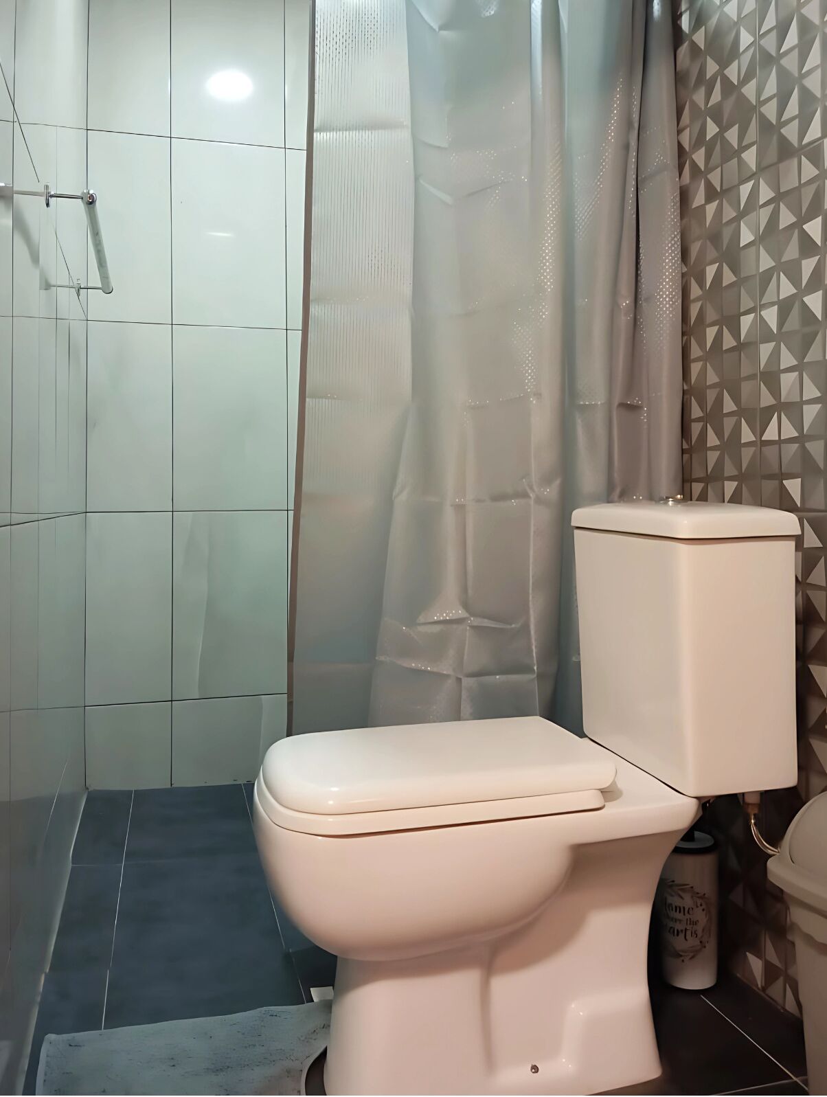A bathroom with a toilet, a shower curtain, and tiled walls.