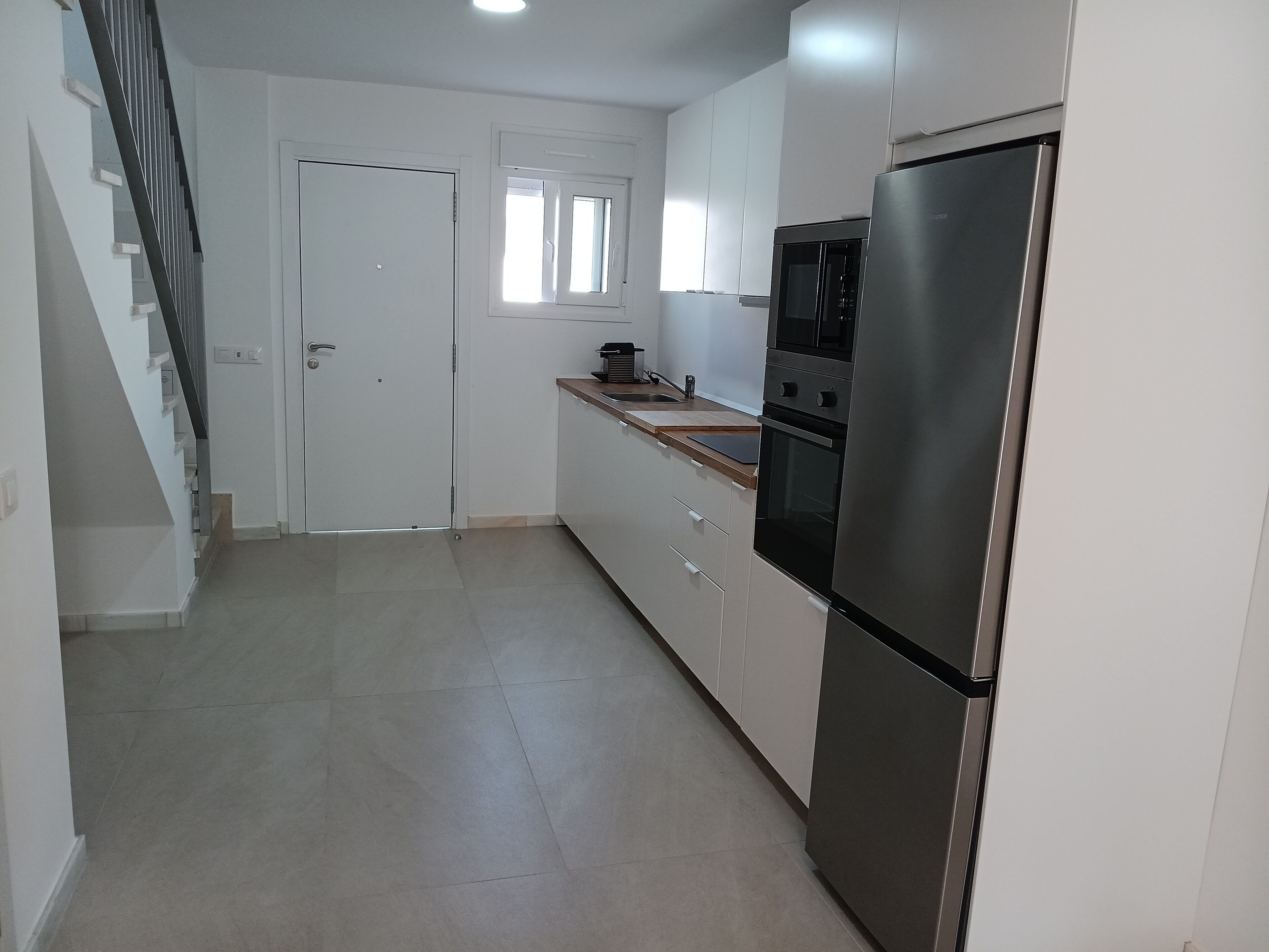 A modern kitchen with white cabinets, a stainless steel refrigerator, and a wooden countertop.