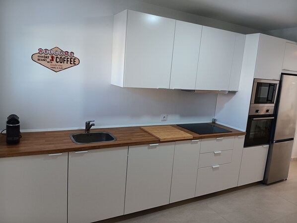 A modern kitchen with white cabinets, a stainless steel refrigerator, and a coffee maker on the counter.