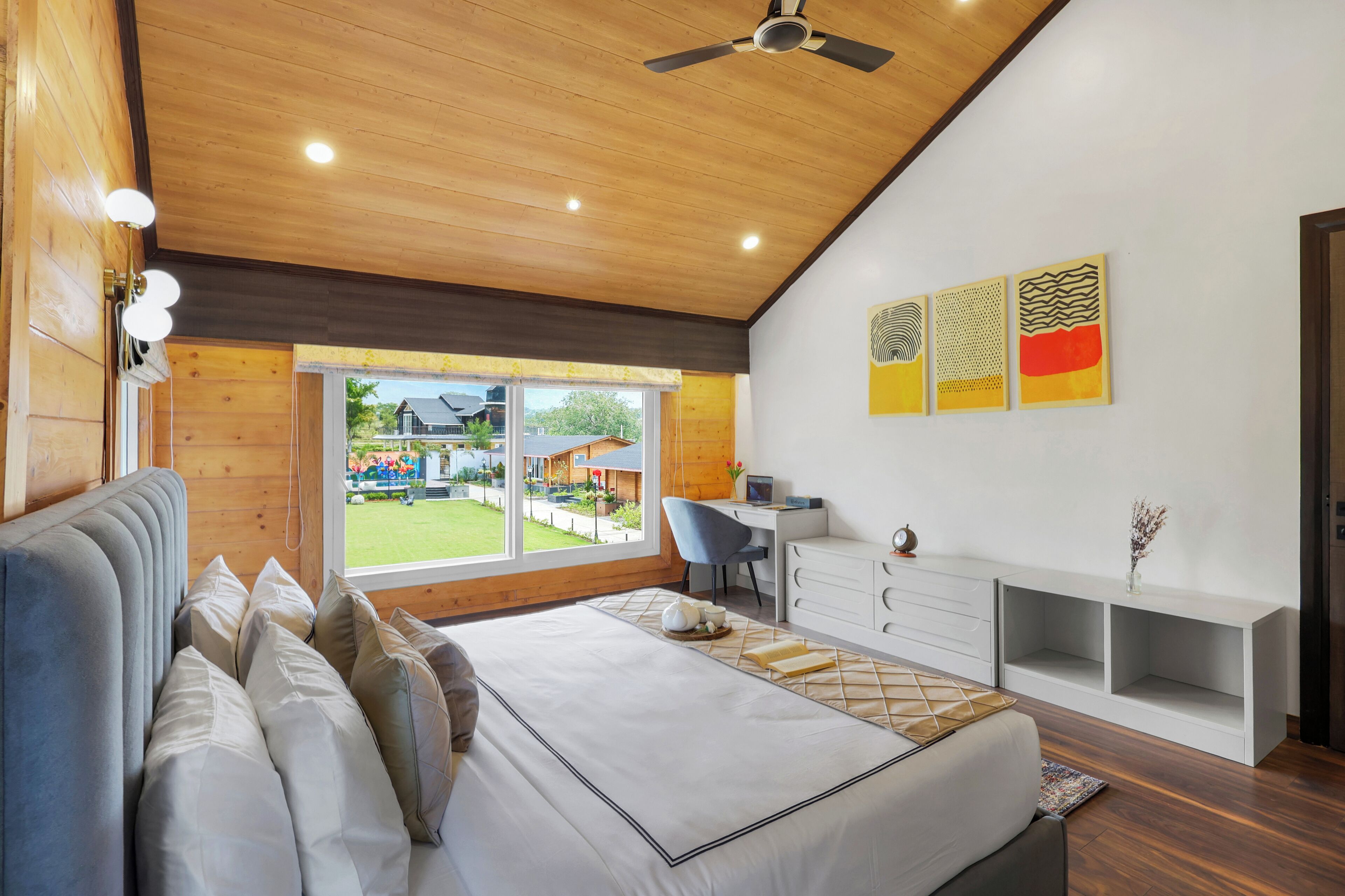A modern bedroom with a large bed, a desk, and a view of the outdoors.