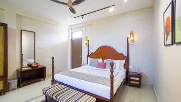 A hotel room with a large bed, a ceiling fan, a bedside table with a lamp, and a bench.
